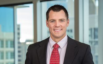 Steven R. Glauser, an Attorney at Parr Brown Gee and Loveless, stands in a high rise office smiling and dressed in a suit