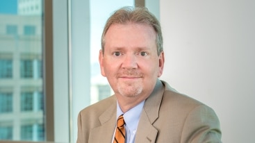 Parr Brown President Daniel A. Jensen sits by a sunny window in a professional suit and smiles at the camera